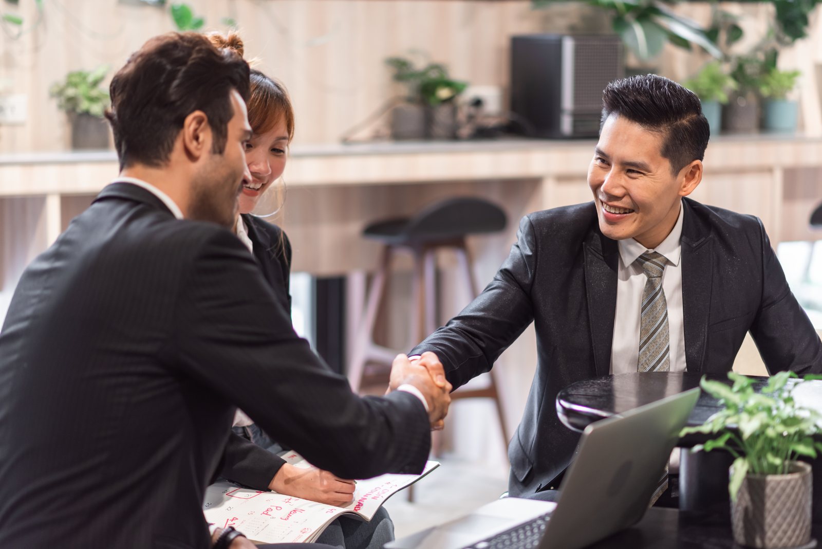 Business team shaking hands over a laptop and paperwork in a modern office after agreeing a deal