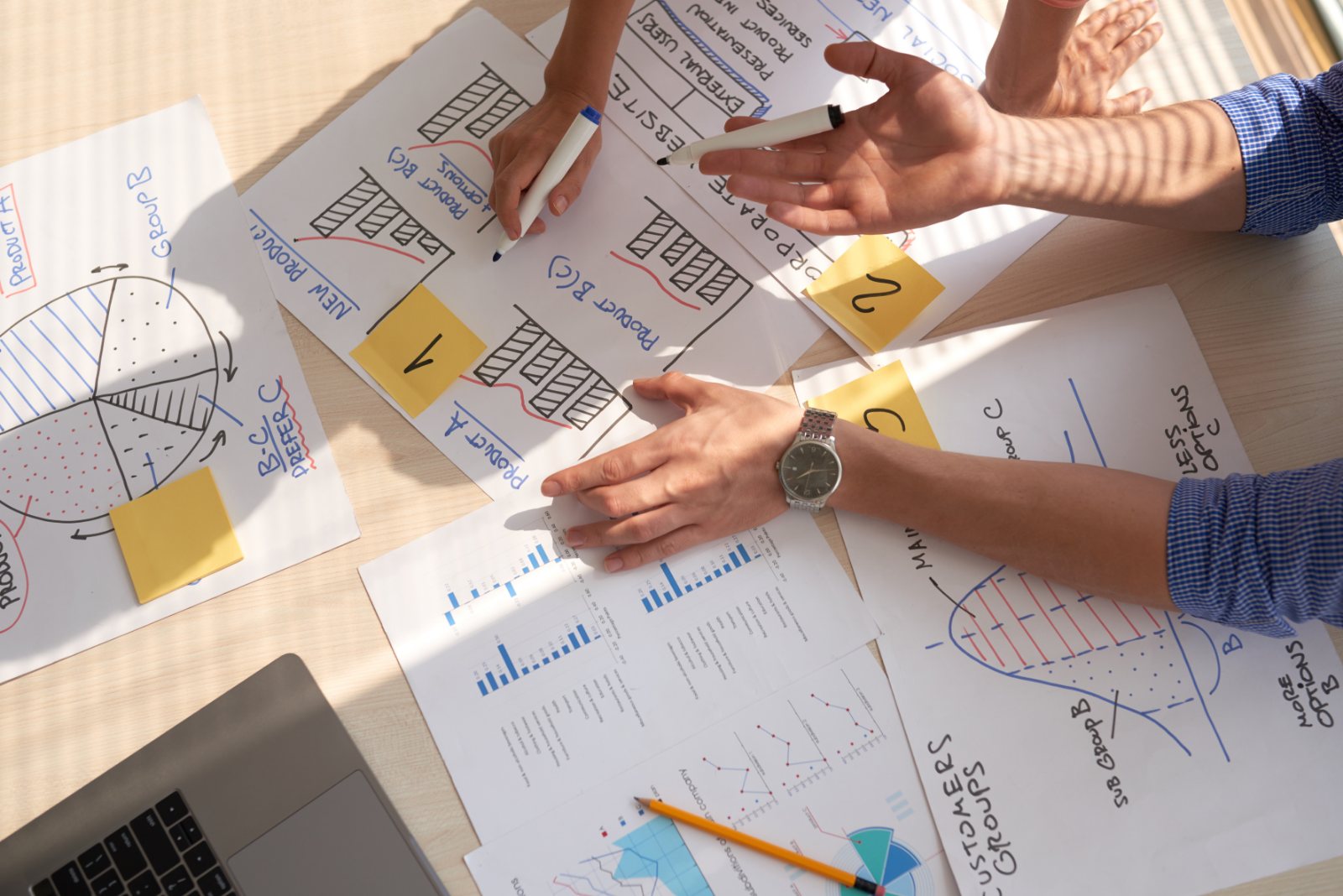 Top view of a marketing team mapping customer segments and demand graphs on paper with marker pens